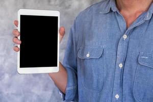 primer plano de un hombre casual que muestra una tableta con pantalla en blanco en el fondo del grunge foto