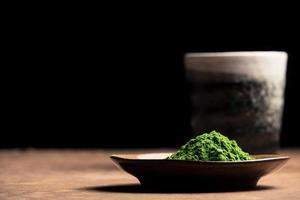 Green tea powder with ceramic cup on the table, black background. Free space for text photo