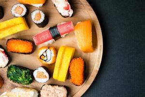 vista superior del sushi en placa de madera sobre fondo negro, comida japonesa. espacio libre para texto