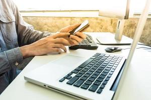 Male hands using smart phone with computer on the desk. photo