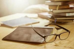anteojos con libros sobre la mesa de madera, enfoque suave, luz solar, tono vintage. foto