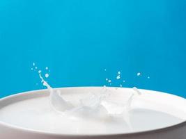 Splash of milk from a cup on blue background. photo