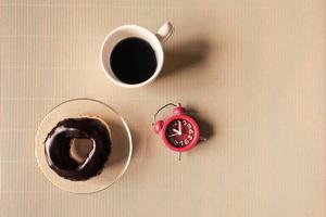 Top view of coffee cup with donut and clock on table. photo