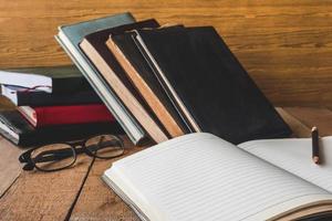 Blank notebook with pencil, glasses and books on wooden table. photo