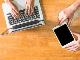 Top view of hands using laptop and tablet on wooden table photo