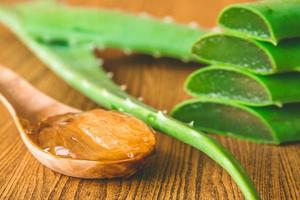 Aloe vera gel on wooden spoon with aloe vera on wooden table. Selective focus photo