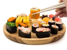 Hand holding sushi roll with chopsticks, Sushi set on wooden plate on white background, Japanese food. photo
