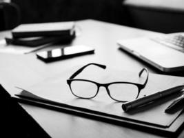Office desk with glasses, documents,laptop,smart phone and notebook. Black and White tone photo