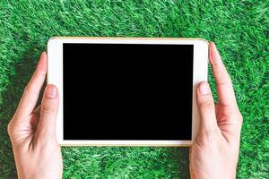 Male hands holding blank digital tablet on green grass background. photo