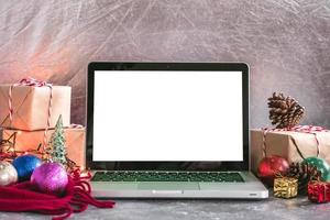 Laptop with white screen, gift boxes and christmas decoration on the table. photo