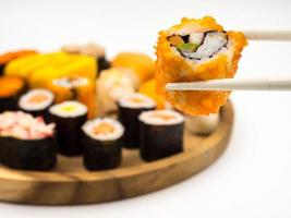 Hand holding sushi roll with chopsticks, Sushi set on wooden plate background, Japanese food. photo
