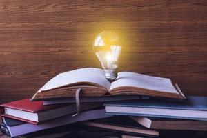 Open book with light bulb and hardback books on wood wall background. Selective focus photo