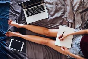 Close up of young woman writing in a book while sitting on her bed,  Films grain filter. photo