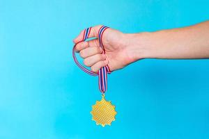 mano sosteniendo la medalla de oro con cinta sobre fondo azul. foto