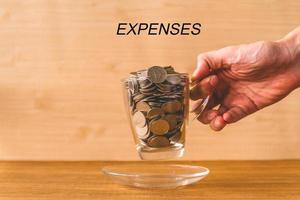 monedas en una taza con texto de gastos en la mesa de madera. concepto financiero. foto