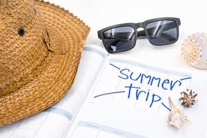 sombrero con gafas de sol, calendario y conchas marinas sobre fondo blanco, concepto de vacaciones de verano foto