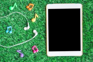 Top view of blank digital tablet with earphones on green grass background. photo