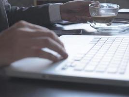 Close up of Businessman drinking coffee and using a laptop on the office desk. photo