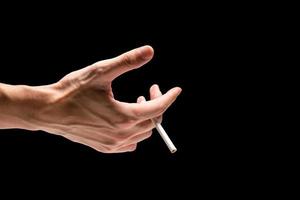 mano masculina sosteniendo un cigarrillo en un fondo negro. foto