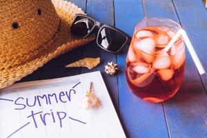 sombrero con gafas de sol, cóctel rojo, calendario y conchas marinas sobre mesa de madera. concepto de vacaciones de verano foto