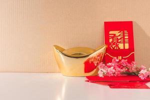 lingotes de oro chinos con paquetes rojos y flores de ciruelo chino sobre la mesa foto