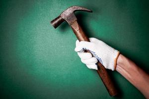 Hammer in hand with protection glove on green background. Free space for text photo