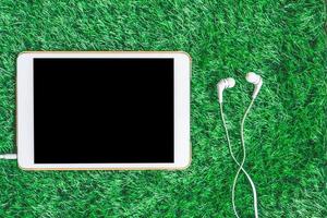 Top view of blank digital tablet with earphones on green grass background. photo