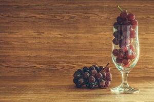 uvas rojas en vidrio sobre la mesa de madera. espacio libre para texto foto