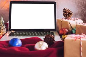 Laptop with white screen, gift boxes and christmas decoration on the table. photo