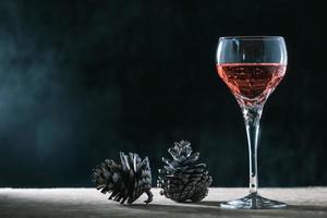 Glass of wine with pine cones on the wooden table, black background, free space for text photo