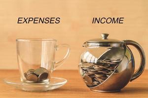 Coins in a cup and a jar on a wooden table, expenses and income text, financial concept photo