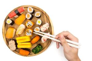 Top view of Sushi set on wooden plate and hand holding chopsticks on white background, Japanese food. photo