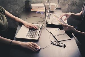 compañeros de trabajo que trabajan en el mismo escritorio, están usando una computadora portátil con tableta, concepto de negocio de inicio, tono vintage foto