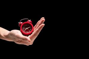 Male hand holding red alarm clock on a black background. Free space for text photo