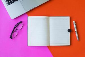 Blank notebook with pen, glasses and laptop on colorful background. photo