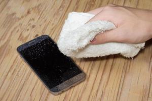 Hands holding White cloth with wet smartphone drops on wooden floor photo