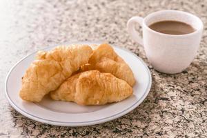 Breakfast with cup of coffee, croissant on the table.