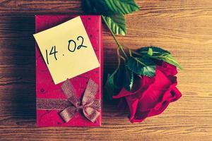 Red gift box with red rose on wooden background. Concept of Valentine Day. photo