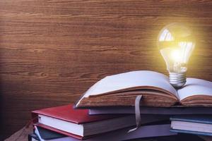 Open book with light bulb and hardback books on wood wall background. Free space for text. Selective focus photo