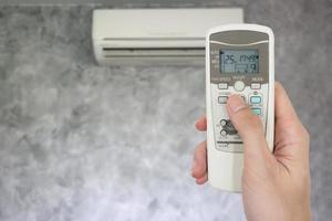 Hand holding remote in front of air conditioner. photo