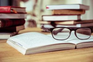 Close up of open book with eyeglasses on wooden desk, Soft focus, Vintage tone photo