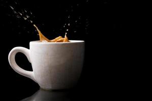 Cup of splashing coffee on black background photo