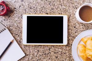 Top view of Tablet with notebook, pencil, clock, coffee and bread on the table photo