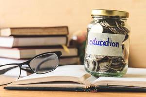 Coins in glass jar with education label, books,glasses and globe on wooden table. Financial concept. photo