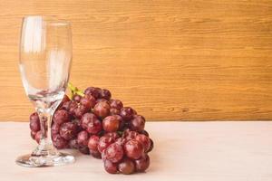 Red grapes with wine glass on the wooden table. Free space for text photo