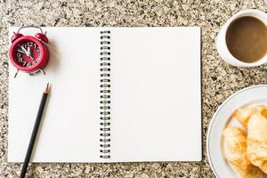 Top view of notebook with pencil, clock, coffee and bread on the table photo