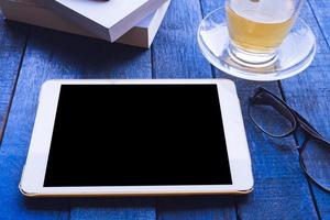 Tablet with glasses,book and tea cup on wooden table photo