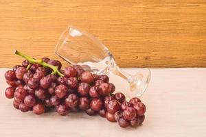 Red grapes with wine glass on the wooden table. Free space for text photo