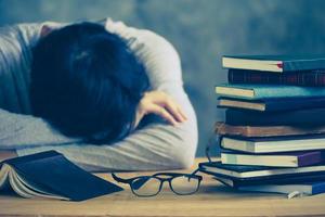 Tired young man sleeping with book stacks on the wooden table. Vintage tone photo