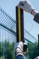 A man measures metal pipes with a tape measure. Construction of the fence. photo